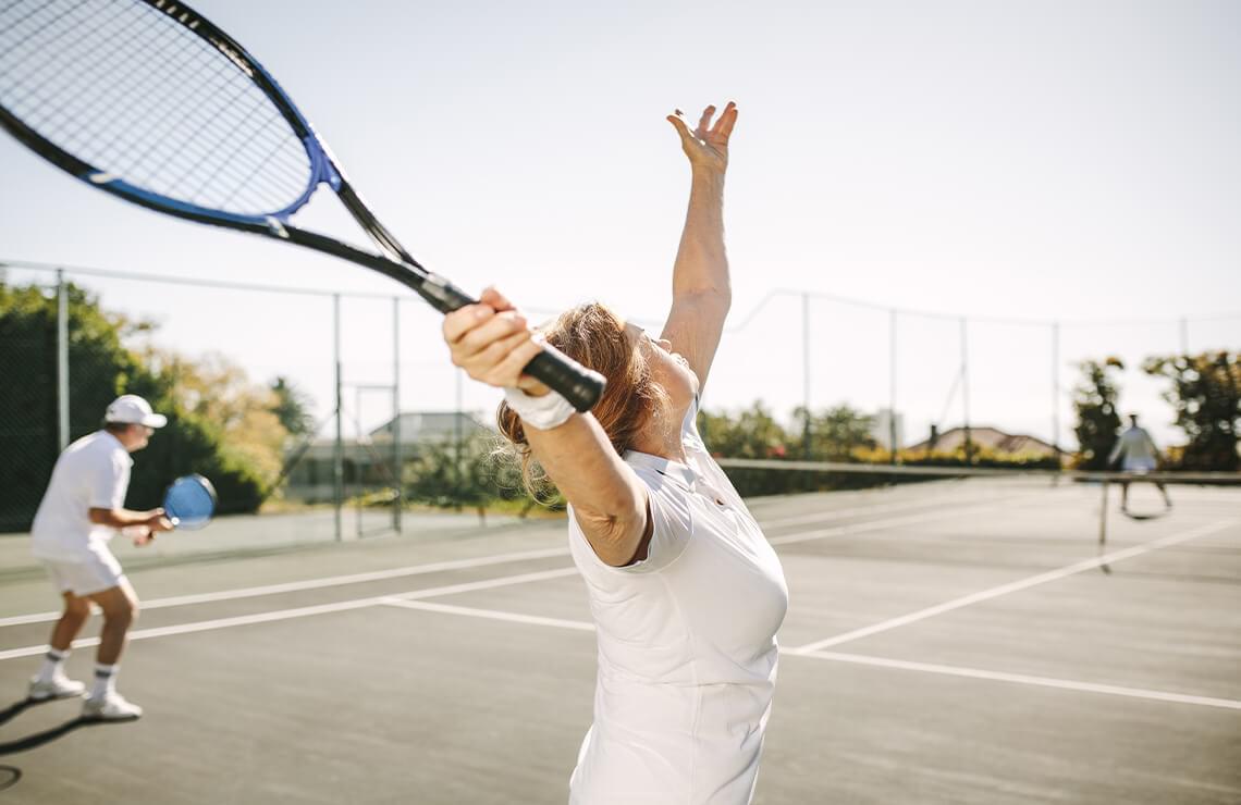 Woman serving tossing tennis ball up to serve