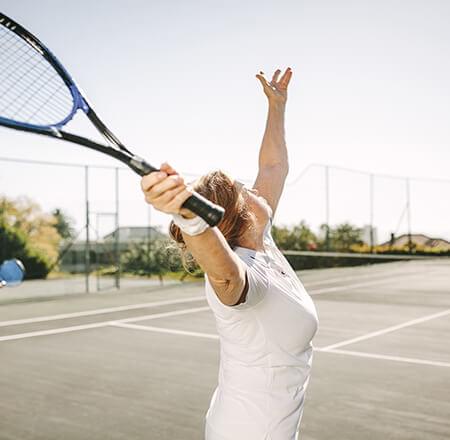 Woman serving tossing tennis ball up to serve