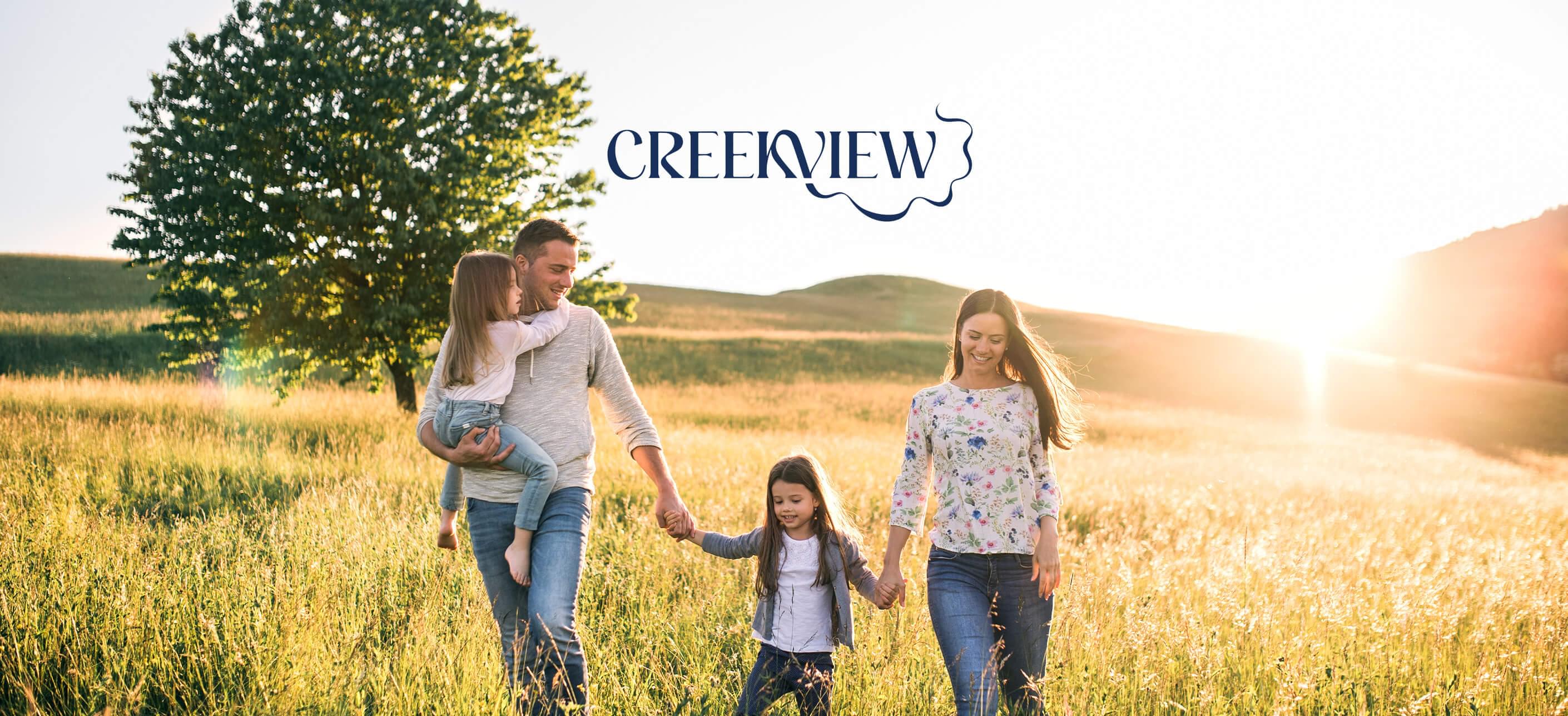 Family of 4 holding hands and walking through field