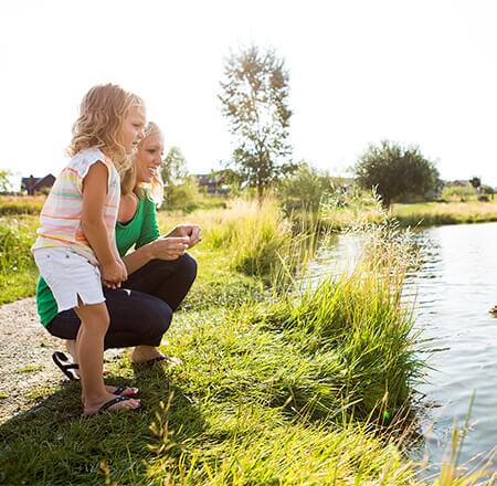 Woman and daughter standing at the edge of a pond